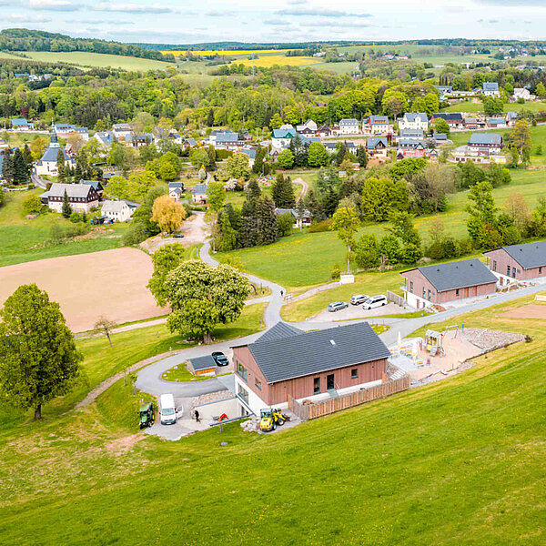 Seiffen Wellnessresort Erlebnisdorf, Drohnenaufnahme auf Hotelanlage am grünen Hang und Stadt Seiffen im Hintergrund