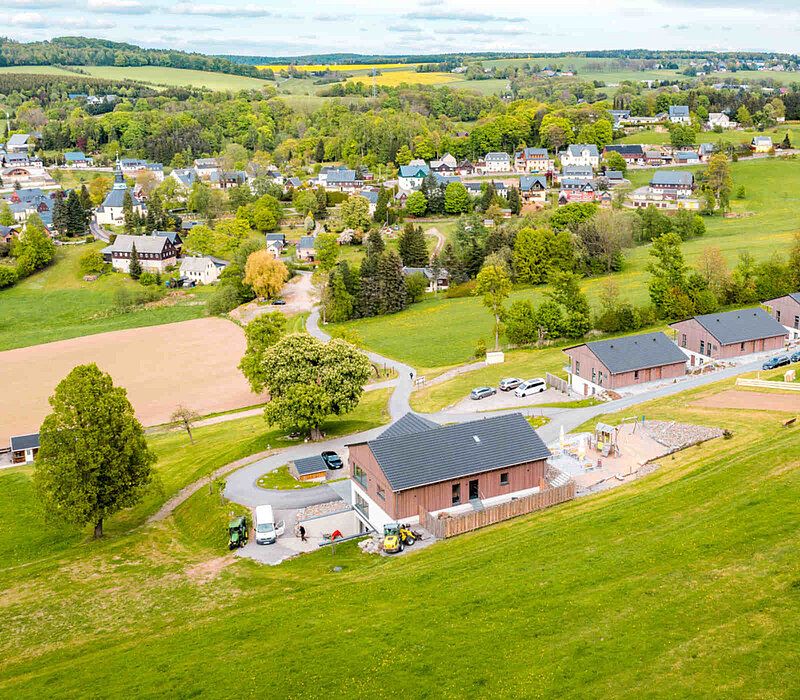 Seiffen Wellnessresort Erlebnisdorf, Drohnenaufnahme auf Hotelanlage am grünen Hang und Stadt Seiffen im Hintergrund
